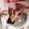 a woman lying on a bed in pretty lingerie with white curtains and a phone