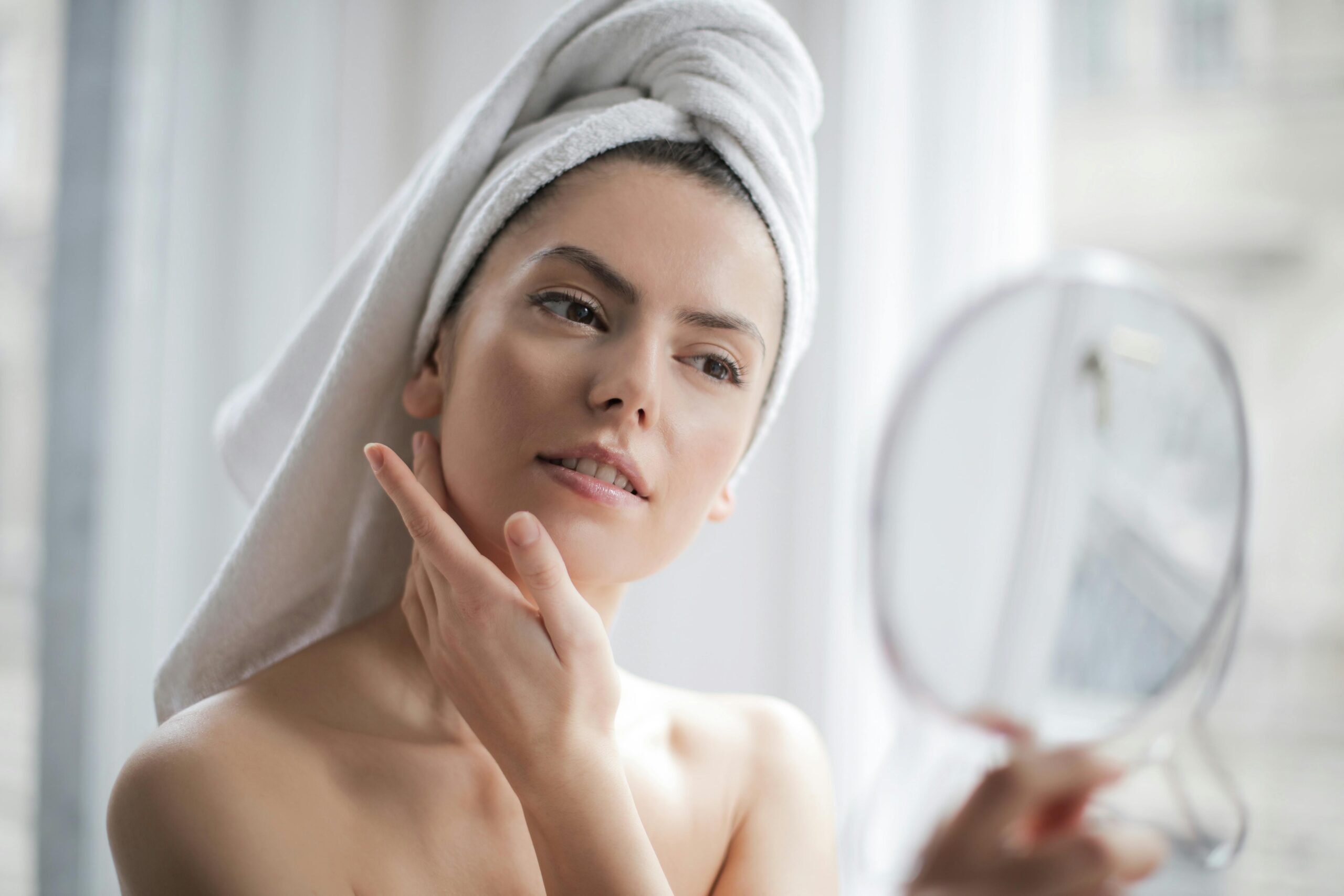 a woman putting skin cream on her face looking into a mirror