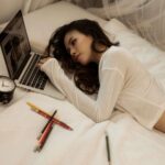 a woman lying on a bed looking at a laptop