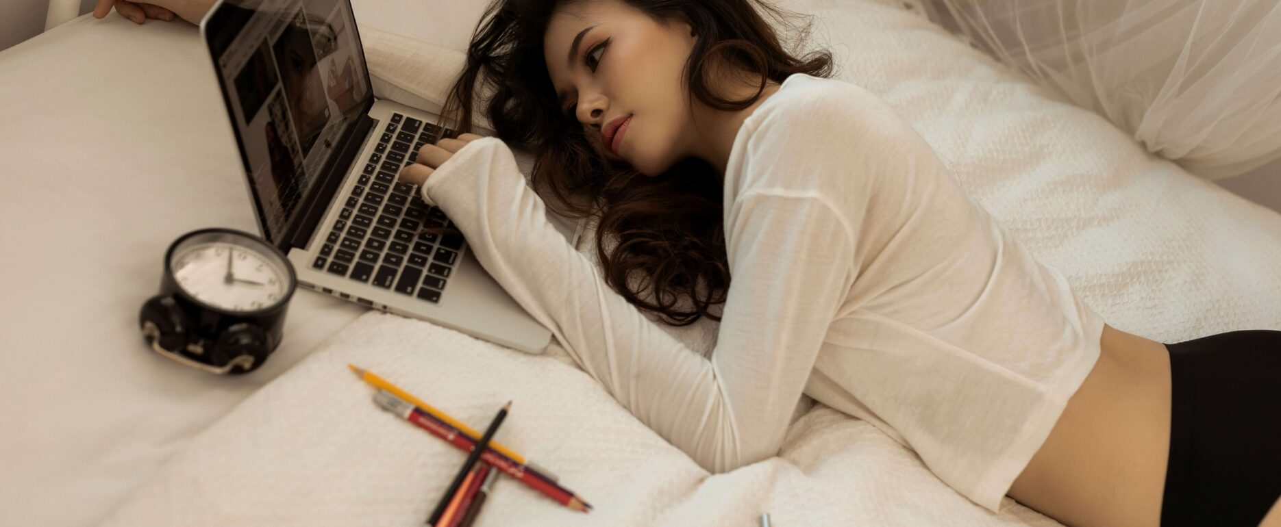 a woman lying on a bed looking at a laptop