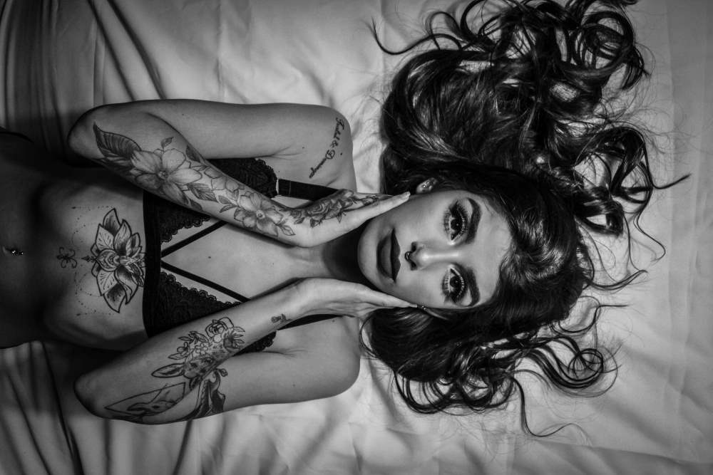 Slim young woman with tattoos lying on bed
